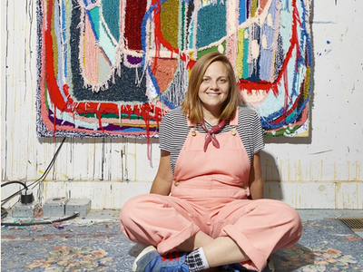 Trish Andersen Fiber Artist in pink jumpsuit in front of fiber carpet painting
